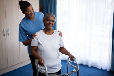 caregiver assisting senior woman in walking with walker